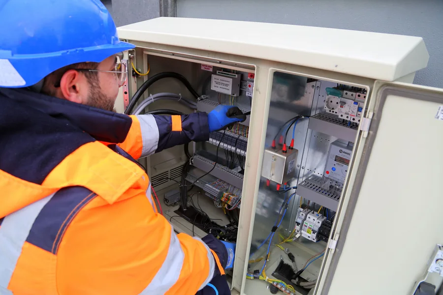 Electricista con casco, gafas y guantes revisando un tablero eléctrico.