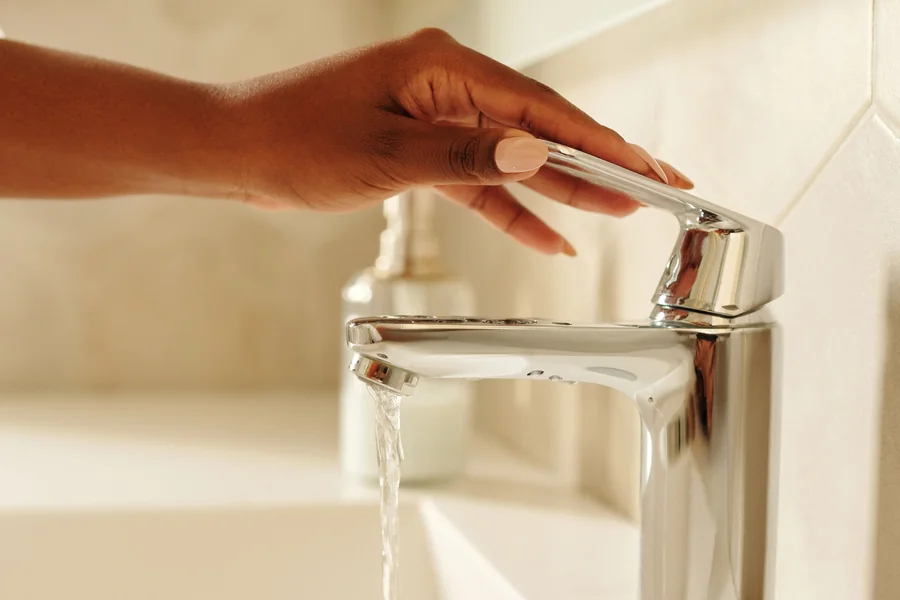 Una mano abre una llave cromada de lavabo con agua corriente.