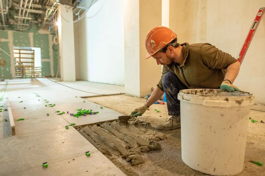 Trabajador con casco extendiendo mortero durante la colocación de losetas de piso.